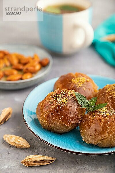 Hausgemachtes traditionelles türkisches Dessert Sekerpare mit Mandeln und Honig  Tasse grüner Tee auf grauem Betonhintergrund und blauem Textil. Seitenansicht  selektiver Fokus