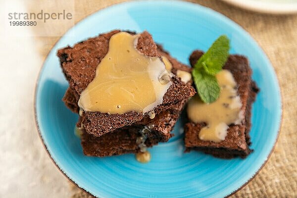 Schokoladen Brownie mit Karamellsauce und einer Tasse Kaffee auf grauem Betonhintergrund und Leinenstoff. Seitenansicht  Nahaufnahme  selektiver Fokus