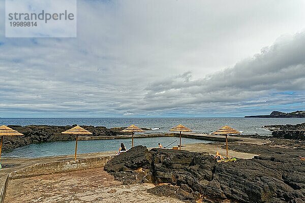 Natürliches Schwimmbad am Meer mit Sonnenschirmen und Menschen  die sich entspannen  Lavafelsen Küstenwanderweg Ponta da Iiha  Calhau  Westküste  Pico  Azoren
