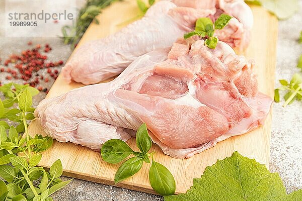 Roher Putenflügel mit Kräutern und Gewürzen auf einem hölzernen Schneidebrett auf einem braunen Betonhintergrund. Seitenansicht  Nahaufnahme  selektiver Fokus