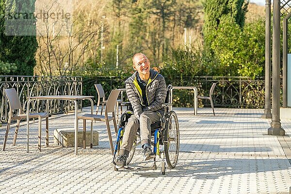 Horizontales Foto mit Weitblick und Kopierraum eines behinderten Mannes im Rollstuhl  der die Sonne im Park genießt
