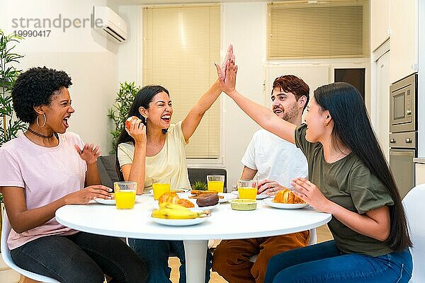 Multiethnische Freunde feiern beim gemeinsamen Frühstück zu Hause und geben sich die Klinke in die Hand