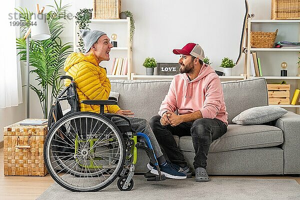 Behinderter Mann im Rollstuhl und Freunde unterhalten sich entspannt im Wohnzimmer des Hauses