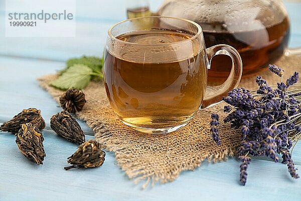 Roter Tee mit Kräutern im Glas auf blauem Holzhintergrund und Leinenstoff. Gesundes Getränk Konzept. Seitenansicht  Nahaufnahme  selektiver Fokus