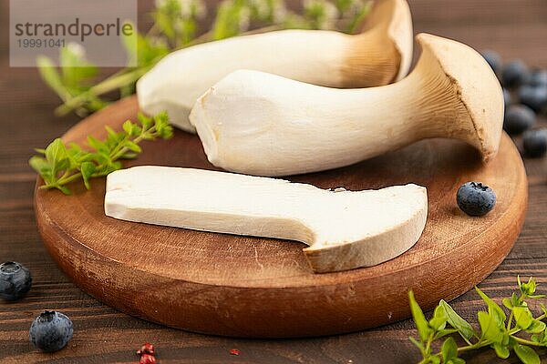 Braune Kräuter Seitlinge (Pleurotus eryngii) auf braunem Holzhintergrund mit Heidelbeeren  Kräutern und Gewürzen. Seitenansicht  selektiver Fokus