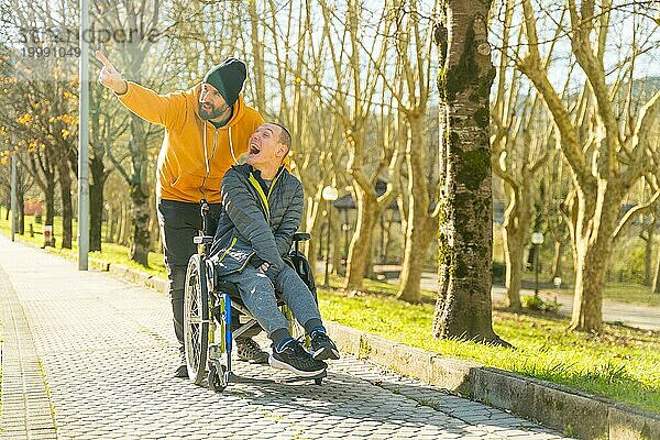 Ein behinderter Mann im Rollstuhl und ein Freund genießen die Natur  indem sie sich in einem Park umsehen