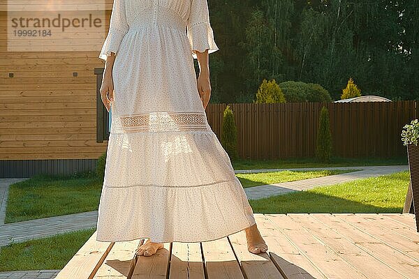 Barfuß Beine einer Frau durch ein dünnes Kleid sichtbar. Unerkennbare Frau auf der Terrasse eines kleinen Hauses