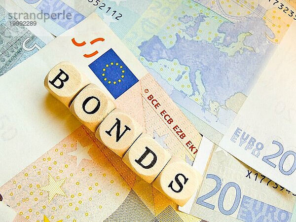 Holzwürfel mit der Aufschrift 'BONDS' auf einem Hintergrund aus Euro-Geldscheinen  Umriss des europäischen Kontinents  Europa auf einem der Banknoten  EU-Flagge  Eurobonds  Buchstabenwürfel  Symbolbild Finanzkrise  Schuldenkrise  Rettungsschirm  Schuldenschnitt  Finanzen  Stabilität  Währungsunion  ESM  EFSF  Verschuldung  Rettungsfonds