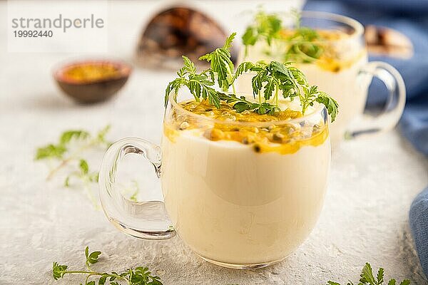 Joghurt mit Passionsfrucht und Ringelblume microgreen im Glas auf grauem Betonhintergrund mit blauem Leinenstoff. Seitenansicht  Nahaufnahme  selektiver Fokus