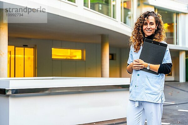 Porträt einer fröhlichen Krankenschwester  die vor dem Krankenhaus steht und in die Kamera lächelt