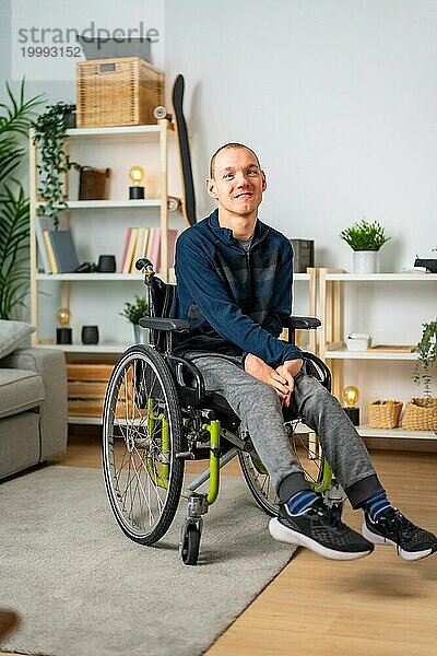 Vertikales Porträt eines glücklichen behinderten Mannes im Rollstuhl zu Hause