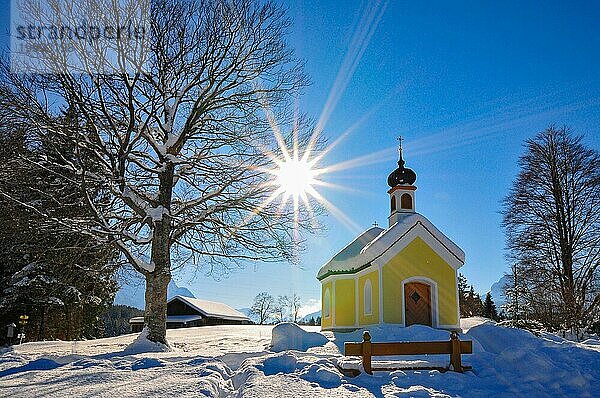 Gegenlichtaufnahme der verschneiten Kapelle Maria auf den Buckelwiesen im Werdenfelser Land bei Garmisch in winterlicher Idylle  Bayern  Deutschland  Europa