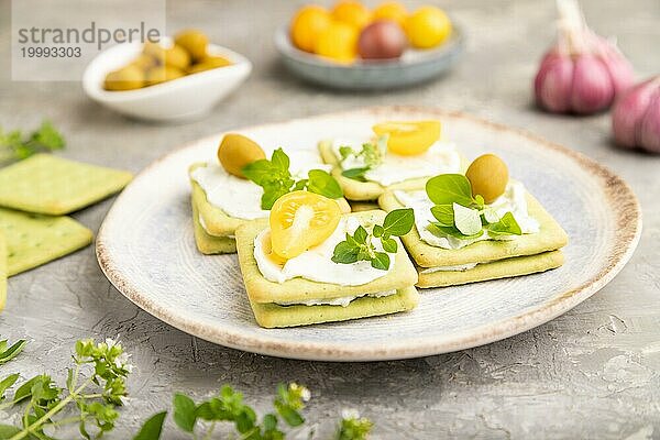 Grüne Cracker Sandwiches mit Frischkäse und Kirschtomaten auf grauem Betonhintergrund. Seitenansicht  Nahaufnahme  selektiver Fokus