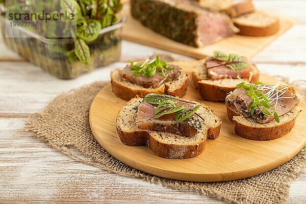 Brotsandwiches mit gesalzenem Dörrfleisch  Sauerampfer und Koriander Mikrogrün auf weißem Holzhintergrund und Leinenstoff. Seitenansicht  Nahaufnahme  selektiver Fokus