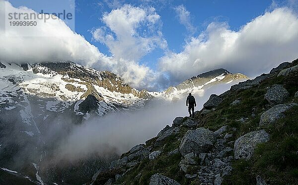 Silhouette eines Bergsteigers vor wolkenverhangener stimmungsvoller Berglandschaft  felsige verschneite Berge mit Gipfel Hochsteller  Furtschaglhaus  Berliner Höhenweg  Zillertaler Alpen  Tirol  Österreich  Europa