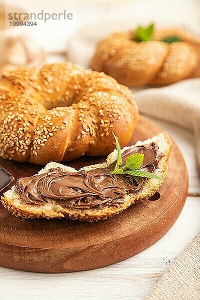 Hausgemachtes süßes Brötchen mit Schokoladencreme und Tasse Kaffee auf weißem Holzhintergrund und Leinentextil. Seitenansicht  Nahaufnahme  selektiver Fokus