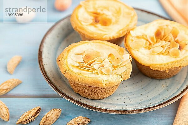 Traditionelle portugiesische Kuchen Pasteis de Nata  Pudding kleine Kuchen mit Mandeln mit Tasse Kaffee auf blauem hölzernen Hintergrund und orange Textil. Seitenansicht  Nahaufnahme  selektiver Fokus