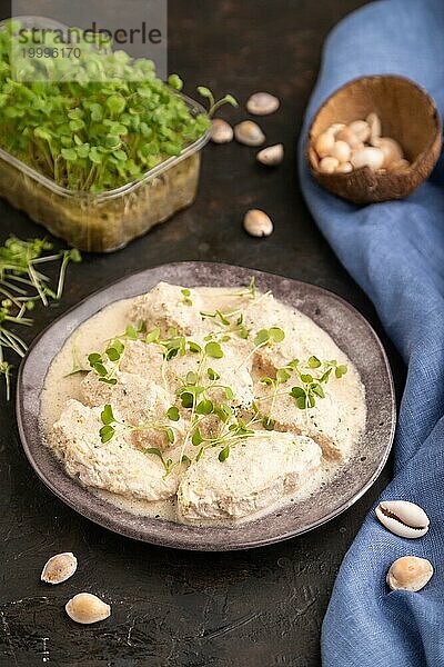 Geschmorte Hühnerfilets mit Kokosmilchsauce und Rucola Mikrogrün auf schwarzem Betonhintergrund und blauem Leinentuch. Seitenansicht  Nahaufnahme  selektiver Fokus