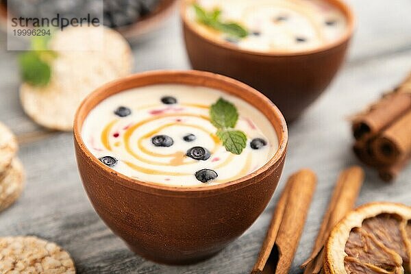 Joghurt mit Heidelbeeren und Karamell in Tonschale auf grauem Holzhintergrund. Seitenansicht  Nahaufnahme  selektiver Fokus