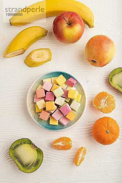 Verschiedene Fruchtgelee Kaubonbons auf einem Teller auf weißem Holzhintergrund. Apfel  Banane  Mandarine  Kiwi  Draufsicht  Flachlage  Nahaufnahme