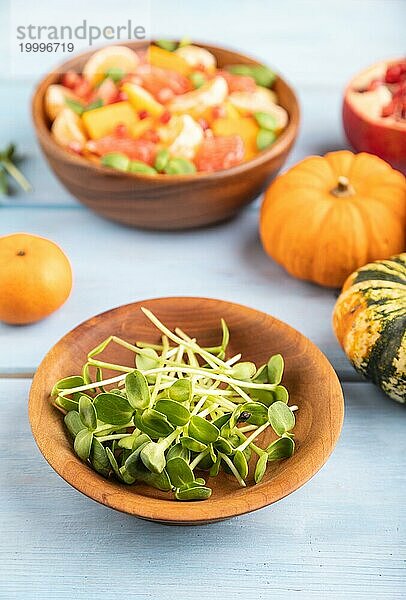 Sonnenblumenmikrosprossen und vegetarischer Obstsalat aus Kürbis  Mandarine  Granatapfel  Grapefruit auf blauem Holzhintergrund. Seitenansicht  Nahaufnahme  selektiver Fokus