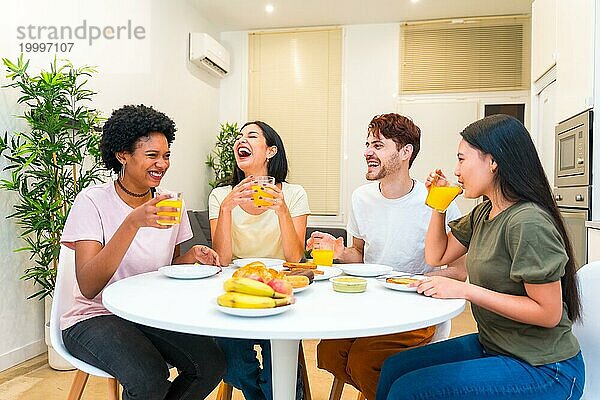 Junge multiethnische Gruppe von Freunden lacht beim gesunden Frühstück zu Hause