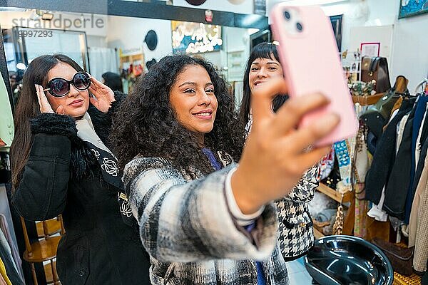 Frontalansicht von drei weiblichen Schönheiten  die ein lustiges Selfie machen  während sie im Verkauf Kleider anprobieren
