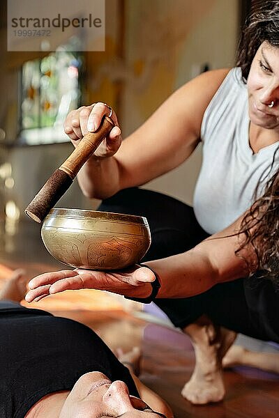 Lateinischer Yogalehrer mit einer Klangschale  die am Ende der Yogastunde für Entspannung sorgt. Vertikales Bild  unscharfer Hintergrund