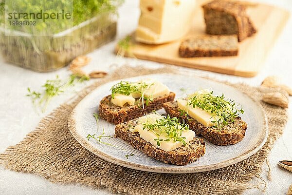 Körnerbrot Sandwiches mit Käse und Brunnenkresse microgreen auf grauem Beton Hintergrund und Leinen Textil. Seitenansicht  Nahaufnahme  selektiver Fokus