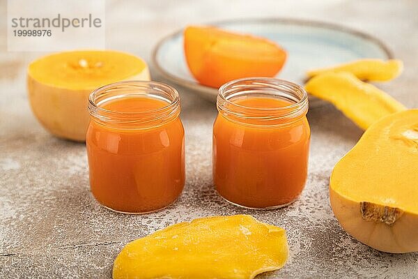 Baby Püree mit Früchten mischen  Kürbis  Kaki  Mango Säuglingsnahrung in Glasgefäß auf braunem Beton Hintergrund. Seitenansicht  Nahaufnahme  selektiver Fokus  künstliche Ernährung Konzept