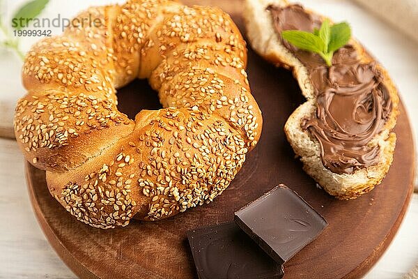 Hausgemachtes süßes Brötchen mit Schokoladencreme und Tasse Kaffee auf weißem Holzhintergrund und Leinentextil. Seitenansicht  Nahaufnahme  selektiver Fokus