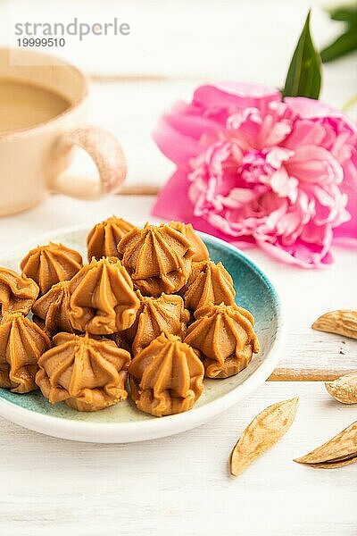 Hausgemachte weiche Karamellbonbons auf blauem Teller und Tasse Kaffee auf grauem Betonhintergrund  Pfingstrose Blumendekoration. Seitenansicht  Nahaufnahme  selektiver Fokus