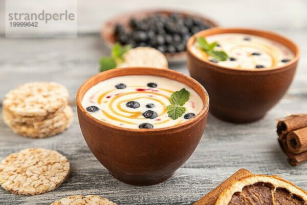 Joghurt mit Heidelbeeren und Karamell in Tonschale auf grauem Holzhintergrund. Seitenansicht  Nahaufnahme  selektiver Fokus