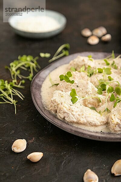 Geschmorte Hühnerfilets mit Kokosmilchsauce und Rucola Mikrogrün auf schwarzem Betonhintergrund und blauem Leinentuch. Seitenansicht  Nahaufnahme  selektiver Fokus