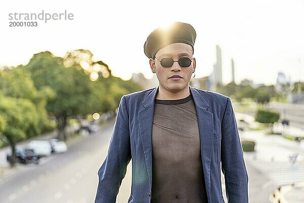 Latino Homosexuell Männchen mit Makeup trägt trendy Hut auf einer Brücke bei Sonnenuntergang