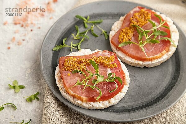 Gepuffte Reiskuchen Sandwiches mit Jerky Salzfleisch  Mikrogrün und Senf auf grauem Betonhintergrund und Leinenstoff. Seitenansicht  Nahaufnahme  selektiver Fokus