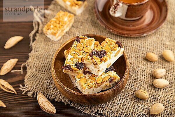 Traditionelle Süßigkeiten Nougat mit Nüssen und Sesam mit Tasse grünem Tee auf braunem Holzhintergrund und Leinenstoff. Seitenansicht  Nahaufnahme  selektiver Fokus