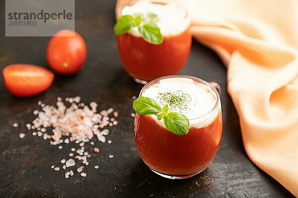 Tomatensaft mit Basilikum  Himalayasalz und saurer Sahne in einem Glas auf einem schwarzen Betonhintergrund mit orangefarbenem Textil. Gesundes Getränk Konzept. Seitenansicht  Nahaufnahme  selektiver Fokus