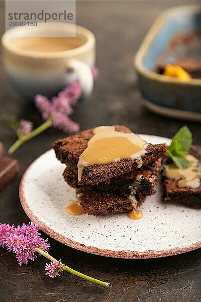 Schokolade Brownie mit Karamell Sauce mit einer Tasse Kaffee auf schwarzem Beton Hintergrund. Seitenansicht  Nahaufnahme  selektiver Fokus