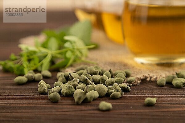 Grüner Oolong Tee mit Kräutern im Glas auf braunem Holzhintergrund und Leinenstoff. Gesundes Getränk Konzept. Seitenansicht  Nahaufnahme  selektiver Fokus