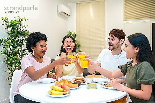 Multiethnische Freunde stoßen morgens beim Frühstück zu Hause mit Orangensaft an