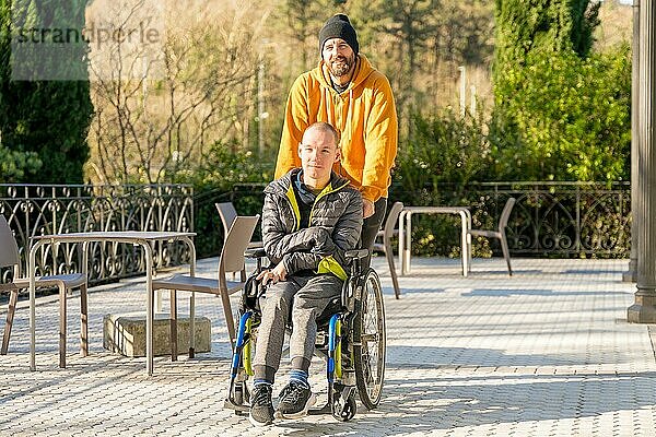 Entspannter behinderter Mann mit Rollstuhl und Freunden bei einem Spaziergang in einem Stadtpark