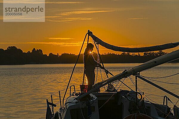 Silhouette einer Frau auf einem Segelboot bei Sonnenuntergang mit orangefarbenem Himmel  Ilinsk-See  Jelonek  Milomlyn  Liebemühl  Ostródzki  Ermland-Masuren  Polen  Europa