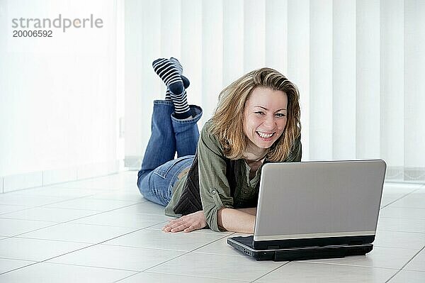 Junge frau liegt mit einem Laptop auf dem Fußboden