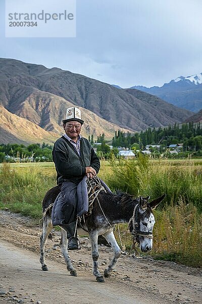 Mann in traditioneller Kleidung reitet auf einem Esel vor einer Bergkulisse  Kirgistan  Asien