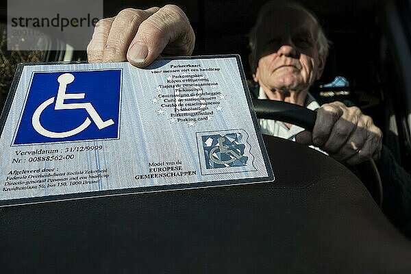Ein behinderter Ã?lterer Mann legt den EU Parkausweis fÃ?r Menschen mit Behinderungen (Blue Badge)  der in der gesamten EU und im EWR einheitlich ist  hinter die Windschutzscheibe eines Autos