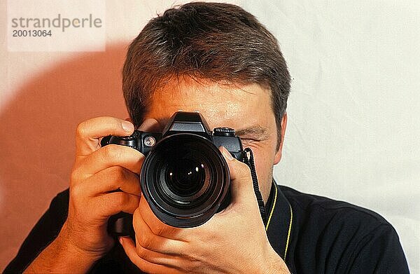 Junger Mann  Fotograf mit Kamera beim Fotografieren  Fokussierung  Porträt  Kamera vor dem Gesicht  Blick durch die Kamera