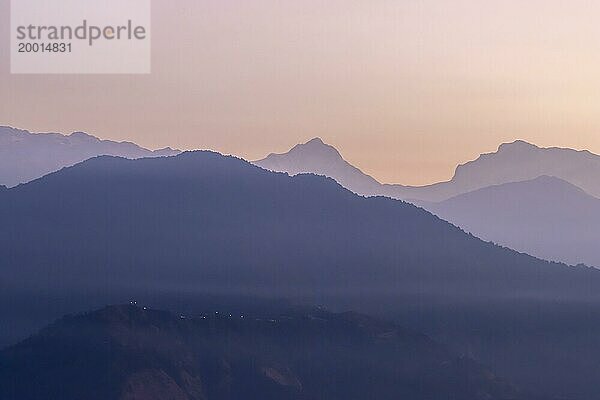 Silhouette des Achttausenders Manaslu und einiger anderer Himalaya Gipfel  darunter Ngadi Chuli  bei Tagesanbruch von Sarangkot  dem beliebten Aussichtspunkt oberhalb von Pokhara  aus einer Entfernung von fast 70 km gesehen. Der klare Januarhimmel leuchtet orange und violett und kontrastiert die Konturen der dunklen Berge. Bezirk Kaski  Provinz Gandaki  Nepal  Asien