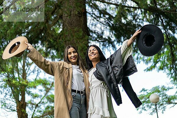 Ein paar Freunde umarmen sich glücklich lächelnd mit Hüten in der Hand im Park