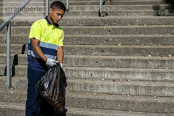 Porträt eines männlichen Latino Müllsammlers in Arbeitsuniform  der Müll von der Straße aufsammelt